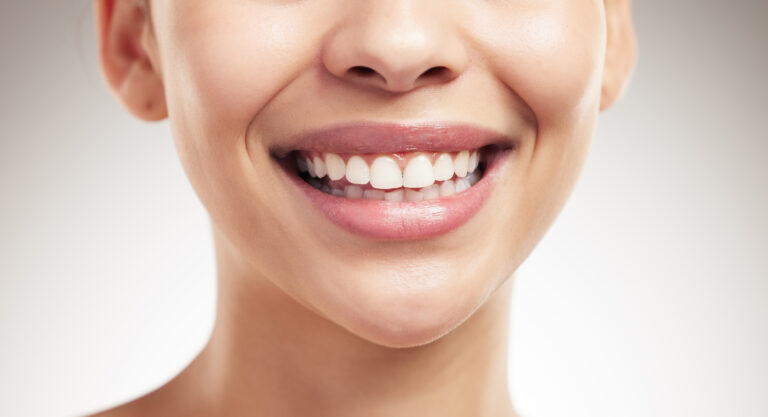 Face of a beautiful woman showing her smile and teeth posing against a grey studio background. Skin.